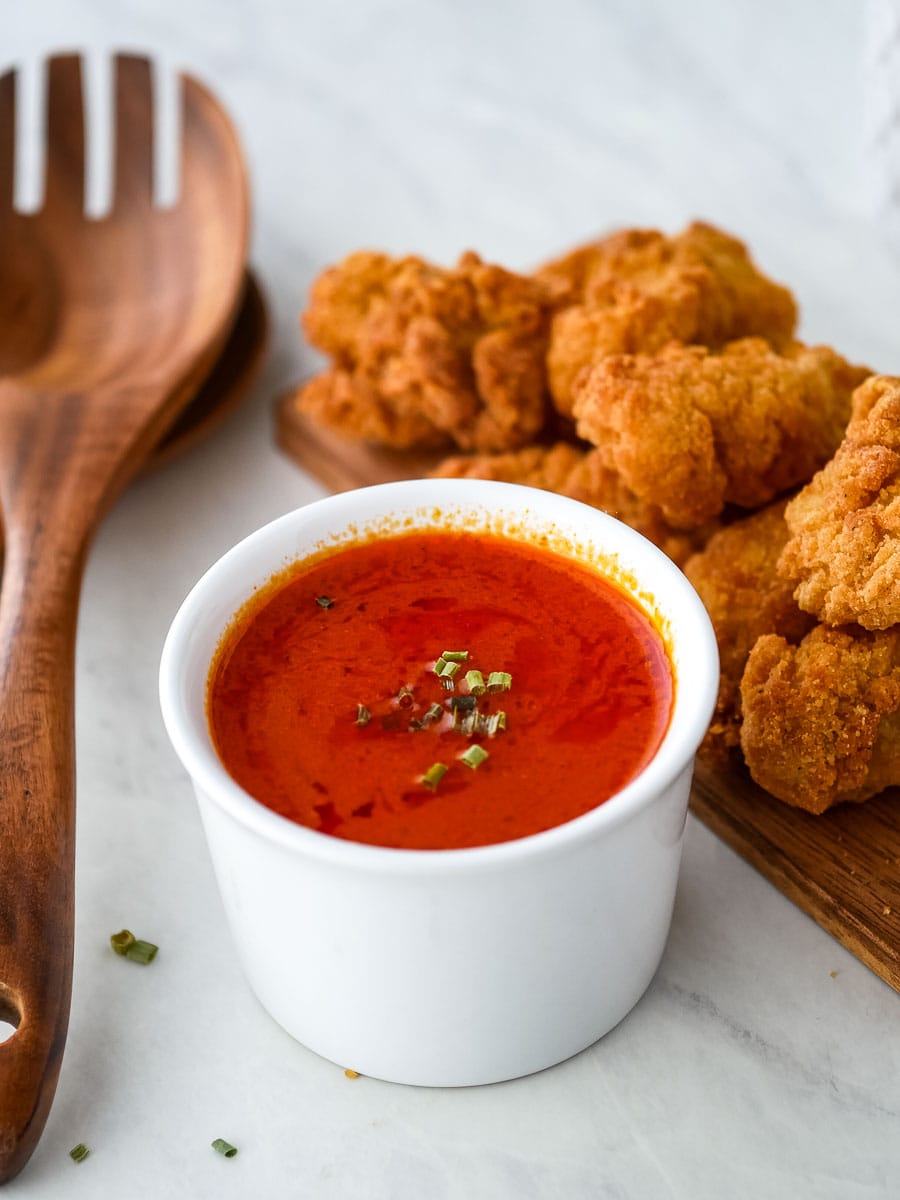 A bowl of chicken nuggets with sauce and a wooden spoon.