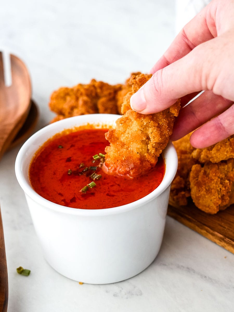 A person dipping chicken wings into a bowl of tomato sauce.