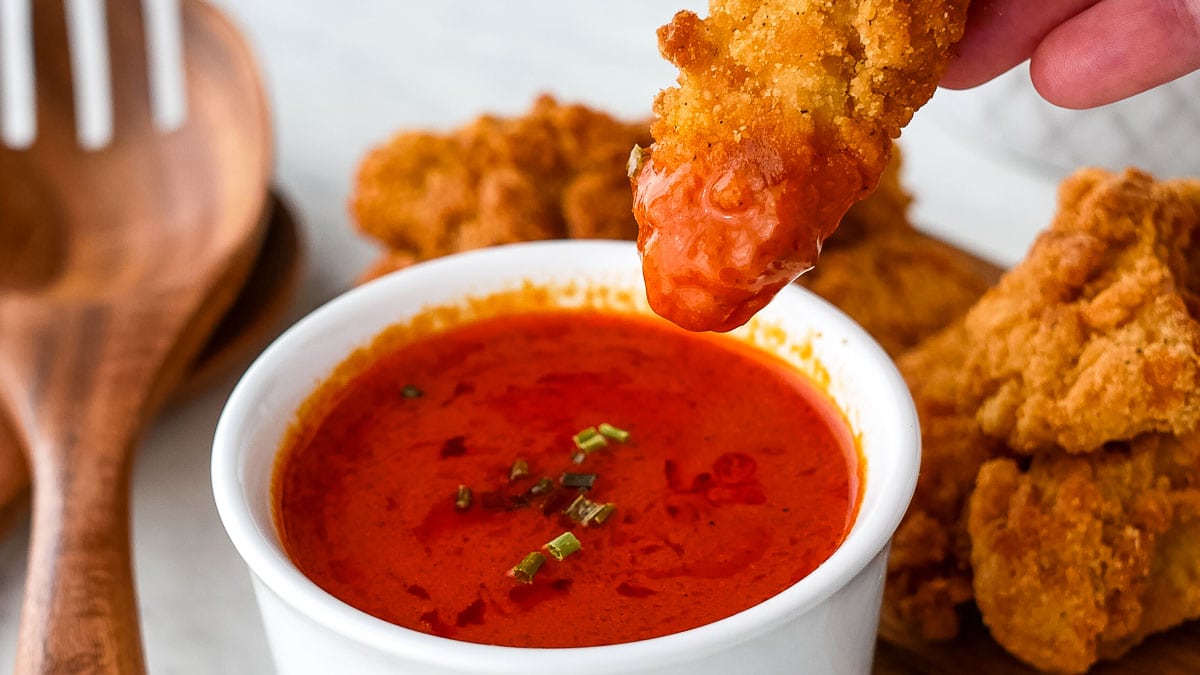 A person is dipping a chicken wing into a bowl of sauce.
