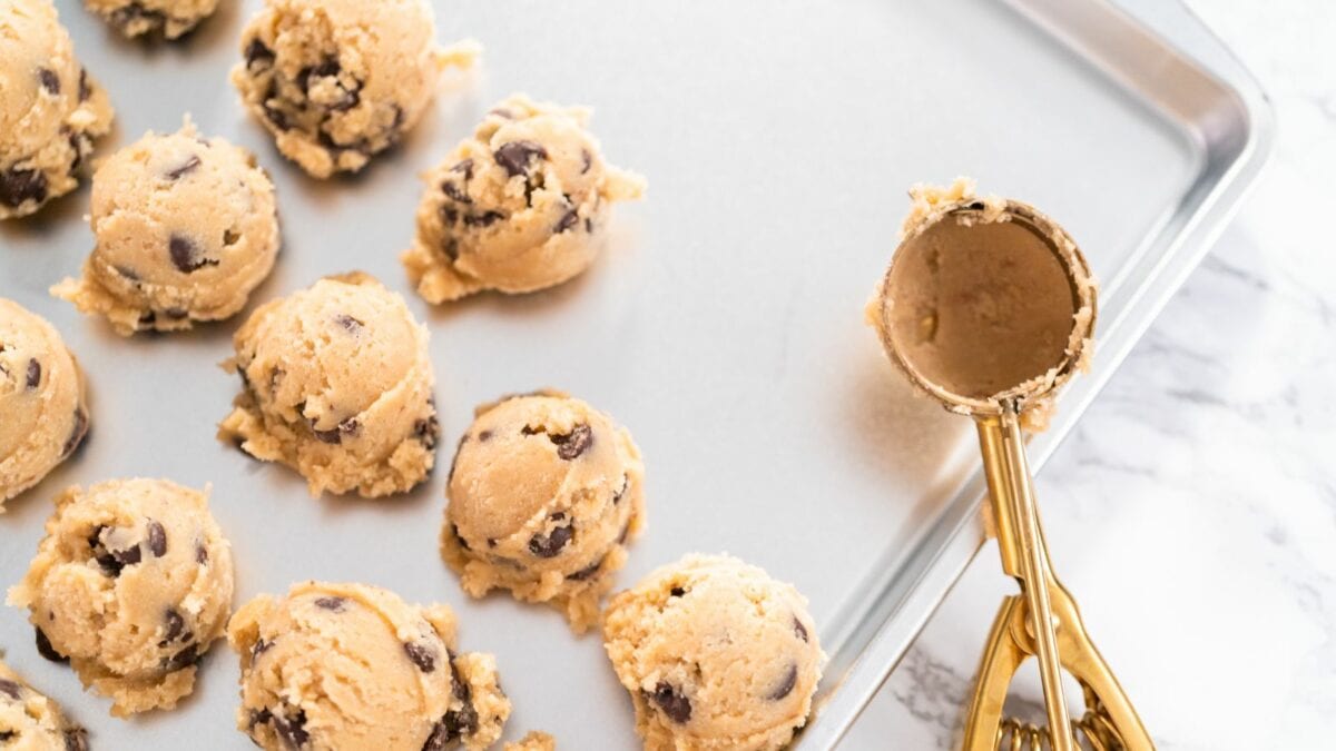 Chocolate chip cookies on a baking sheet with a scooper.