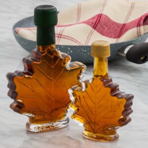 Two maple leaf shaped bottles of maple syrup on a marble counter.