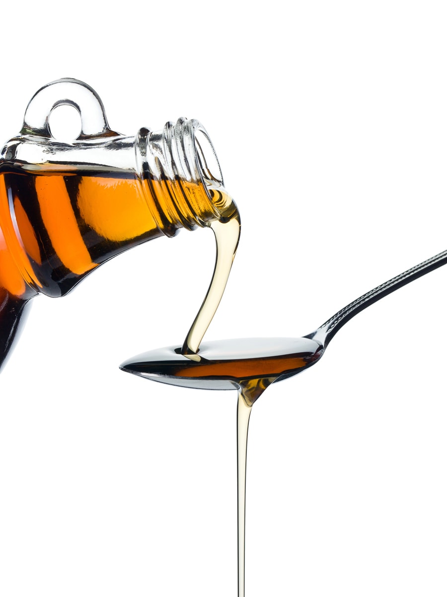 A bottle of maple syrup is being poured into a spoon.