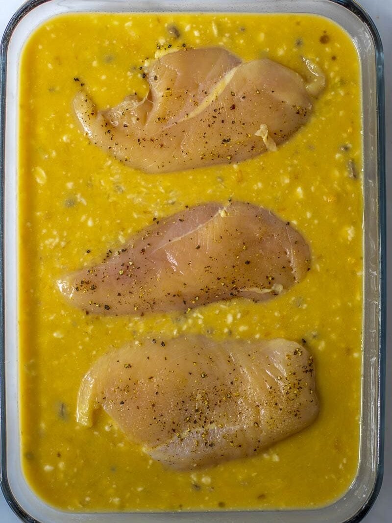 Chicken breasts in a baking dish with a yellow sauce.