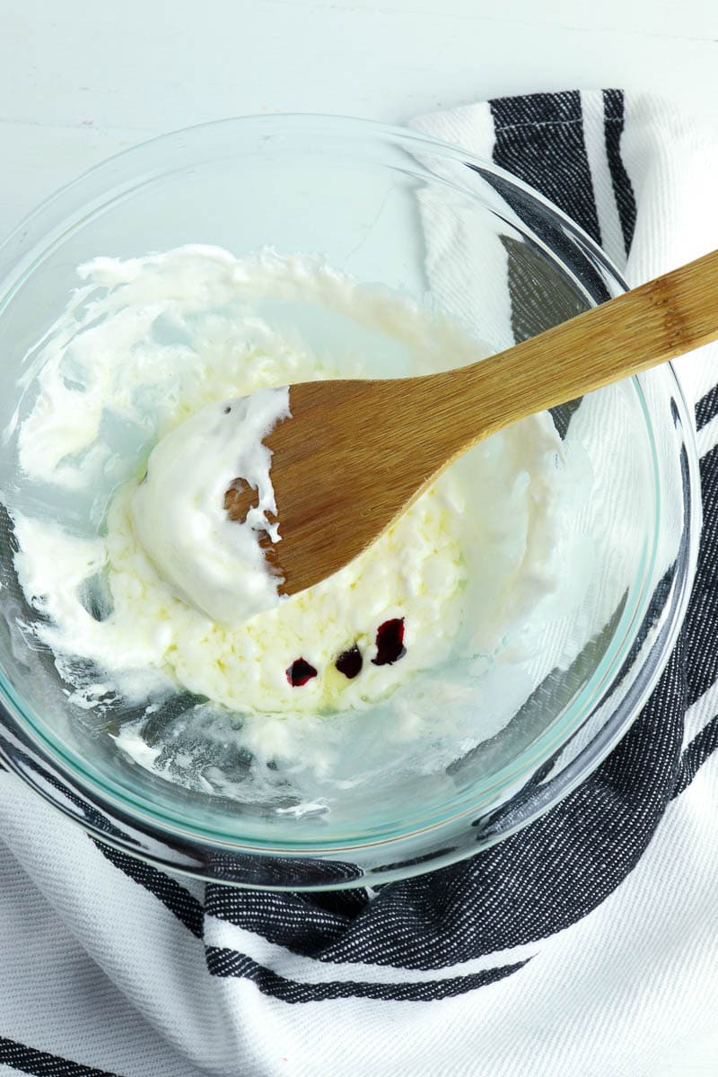 A bowl of whipped cream with berries and a wooden spoon.