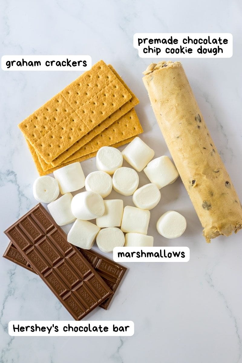 Ingredients for s'mores and chocolate chip cookies laid out on a marble surface.