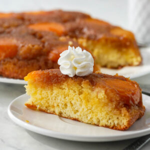A slice of Apricot Upside Down Cake with whipped cream on a white plate.