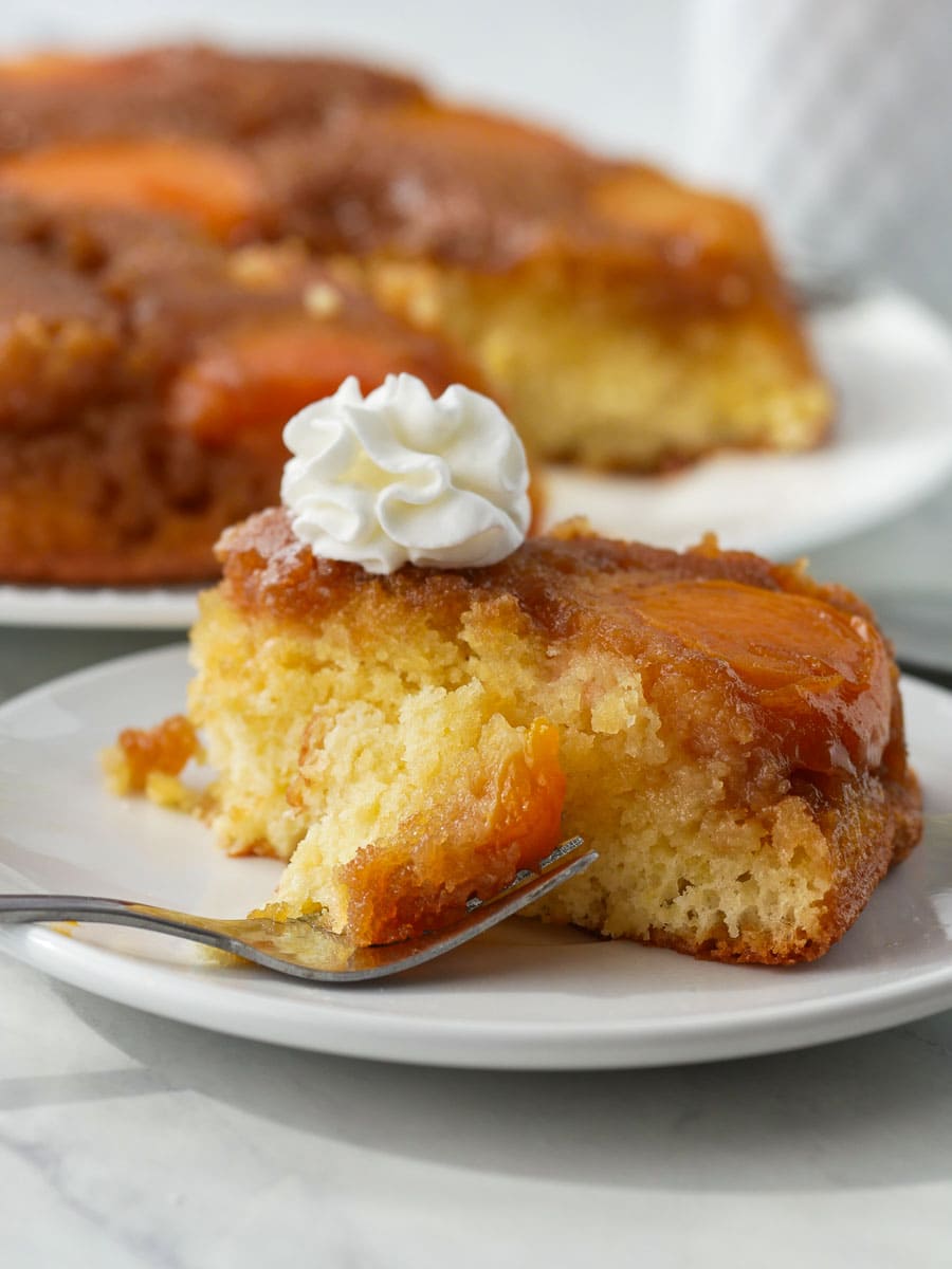 A slice of Apricot Upside Down Cake topped with whipped cream, served on a plate with a fork.