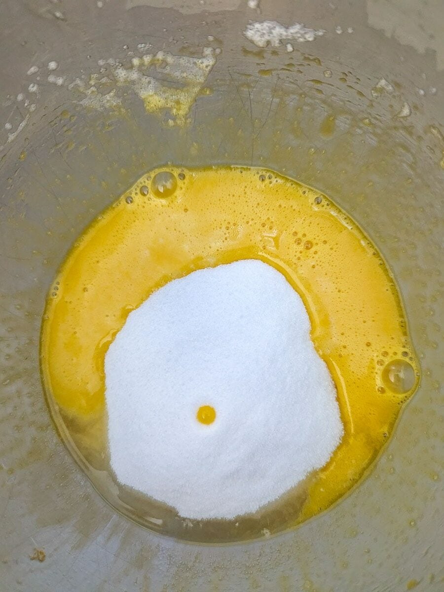 Beaten eggs with a mound of sugar in a mixing bowl.