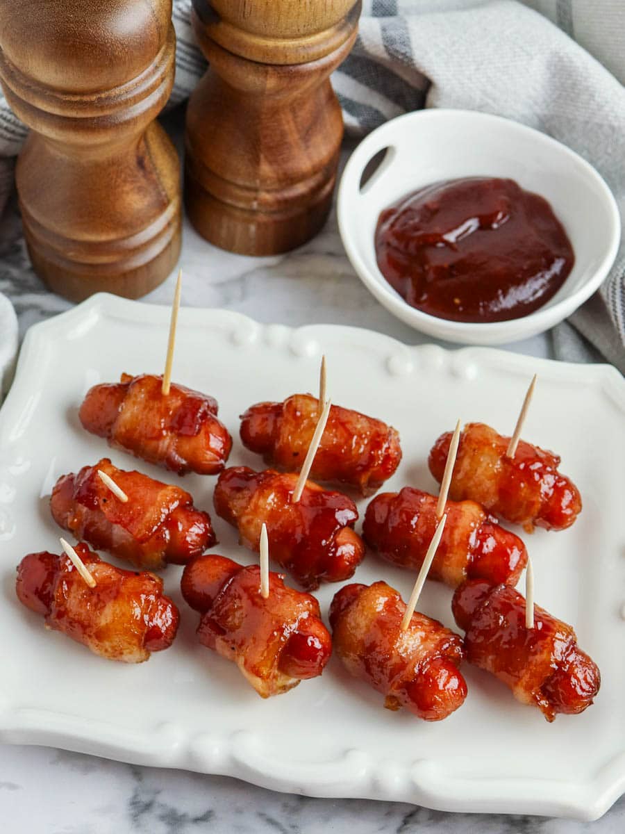 bacon wrapped little smokies on a plate with bbq sauce.