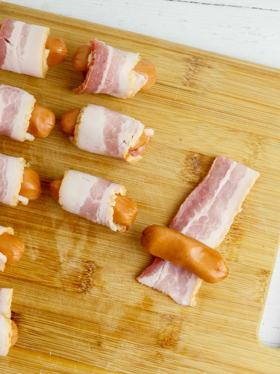 Bacon wrapped little smokies on a cutting board.