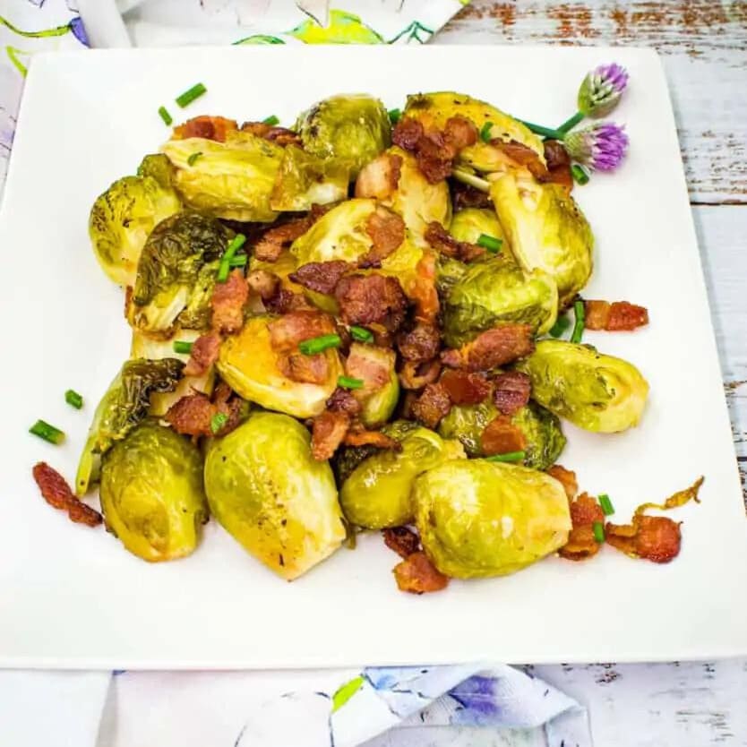 A plate of roasted brussels sprouts garnished with bacon pieces.