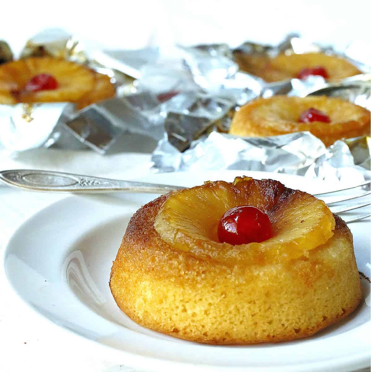 Individual pineapple upside-down cakes with cherries on top, presented on a white background.