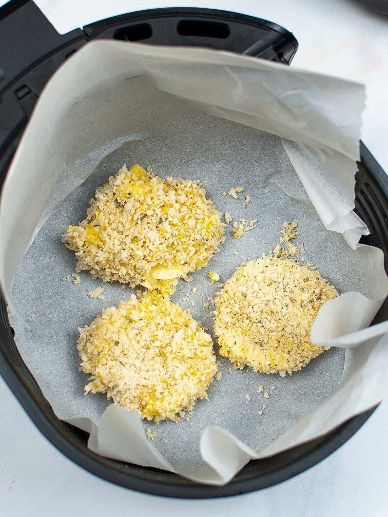 Breaded fried mozzarella placed on parchment paper inside an air fryer basket.