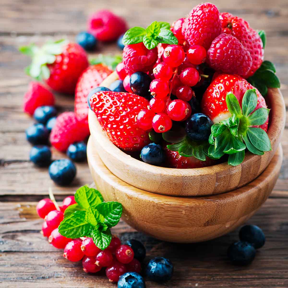 A bowl of mixed fresh berries with mint leaves on a wooden surface.