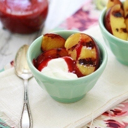 A bowl of yogurt topped with grilled fruit and a drizzle of sauce.
