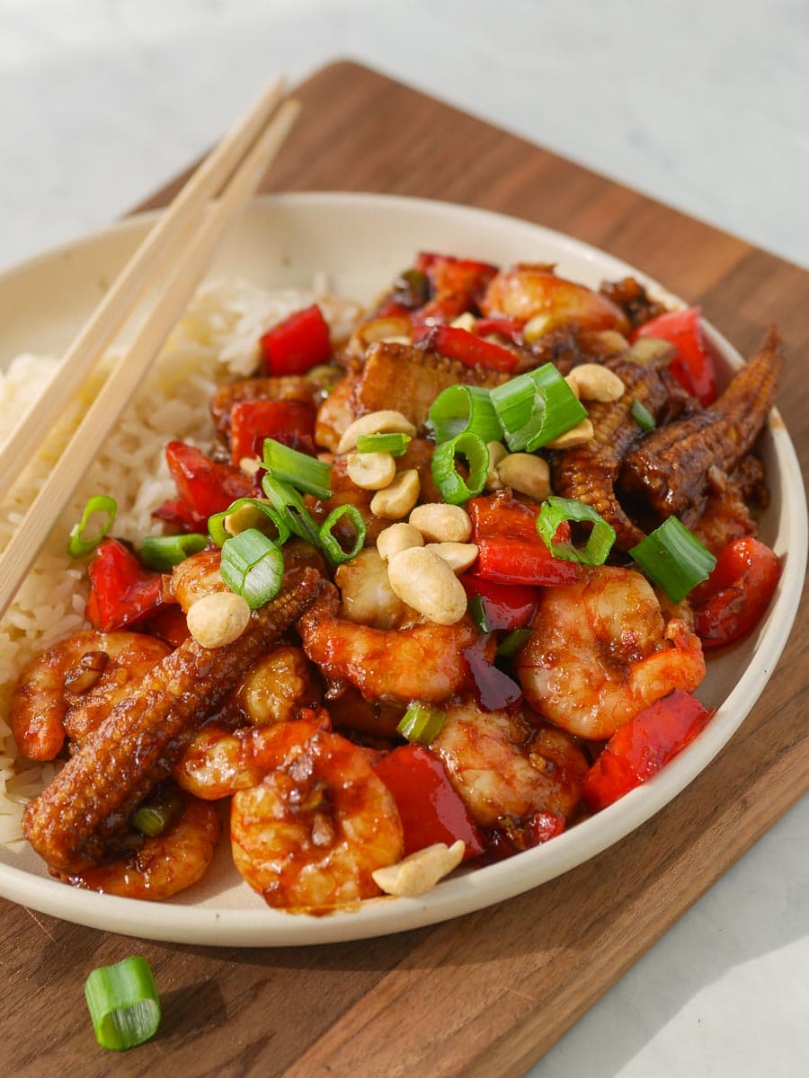 Bowl of kung pao shrimp with vegetables, peanuts, and rice served with chopsticks.