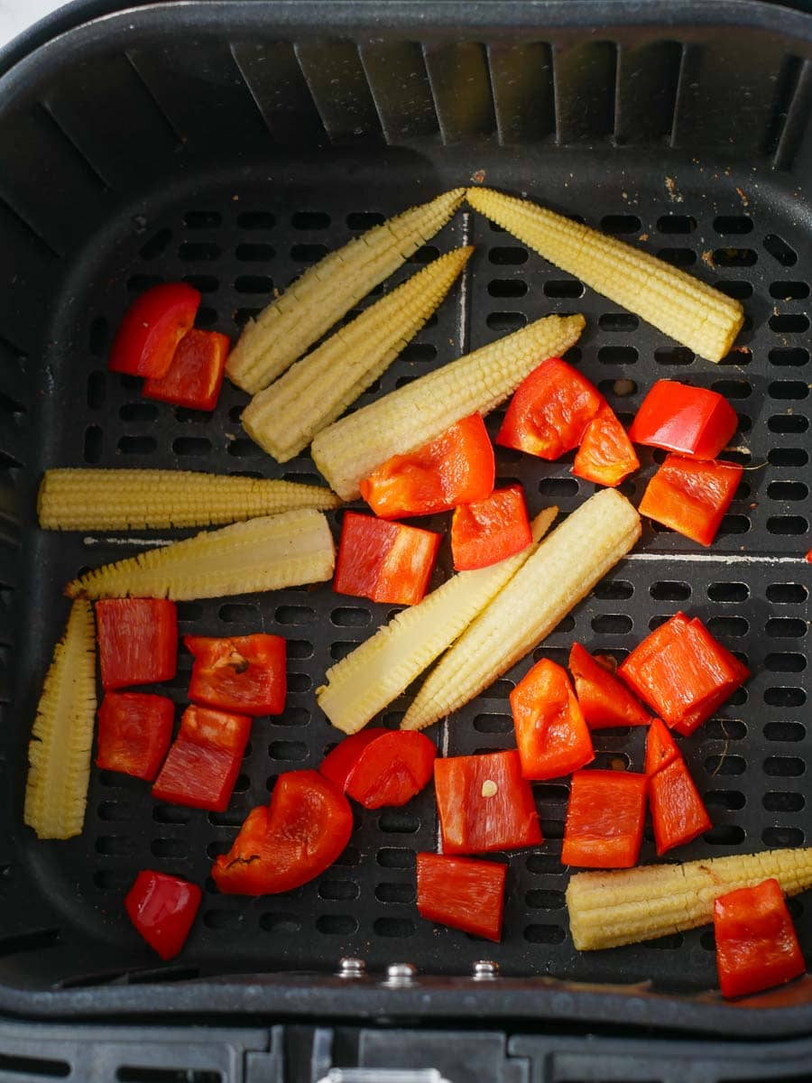 Chopped red bell peppers and baby corn in an air fryer basket.