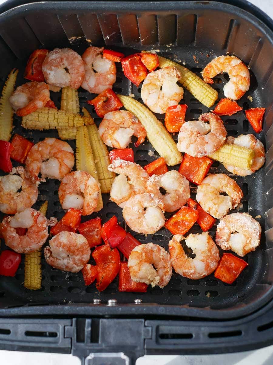 Cooked shrimp, red bell pepper pieces, and baby corn in an air fryer basket.