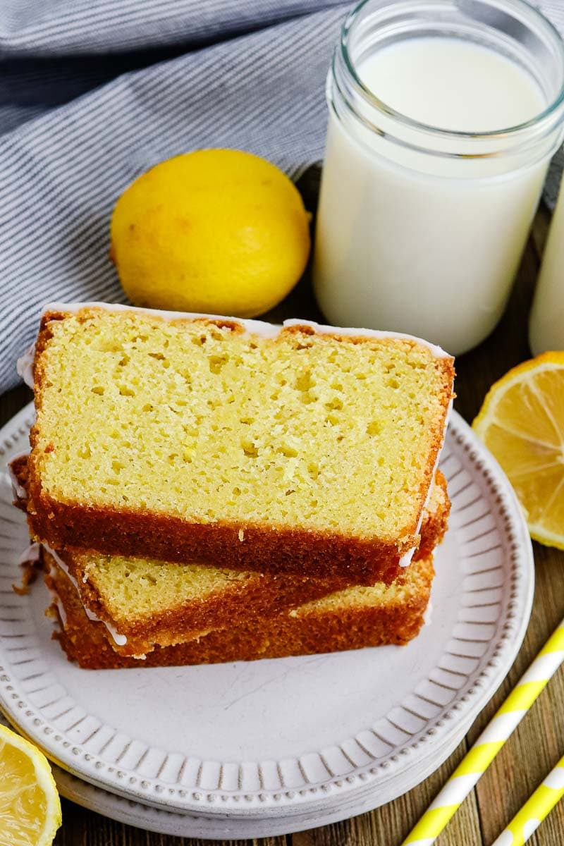 A slice of lemon loaf on a plate next to a glass of milk.