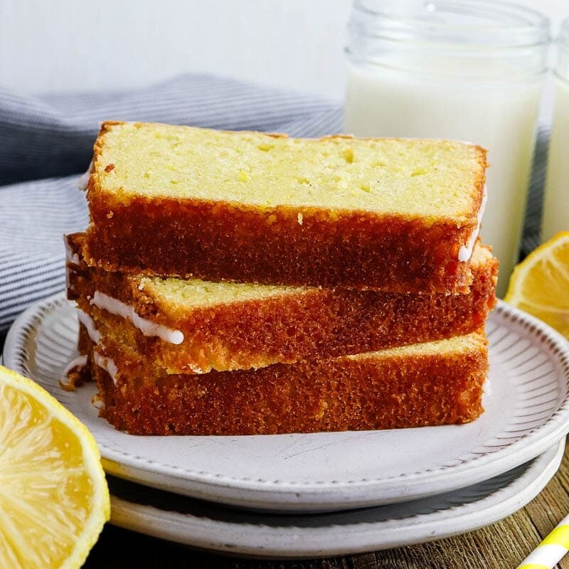 A slice of lemon loaf on a plate next to a glass of milk.