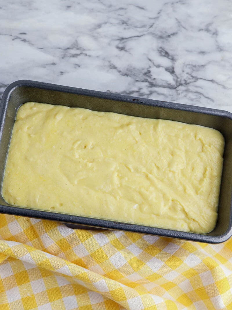 A yellow cake in a pan on top of a yellow checkered tablecloth.