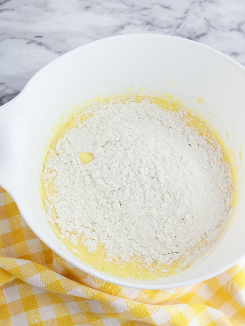 A white bowl filled with flour on a yellow checkered tablecloth.