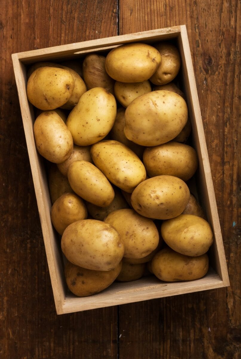 Potatoes in a wooden box on a wooden table.