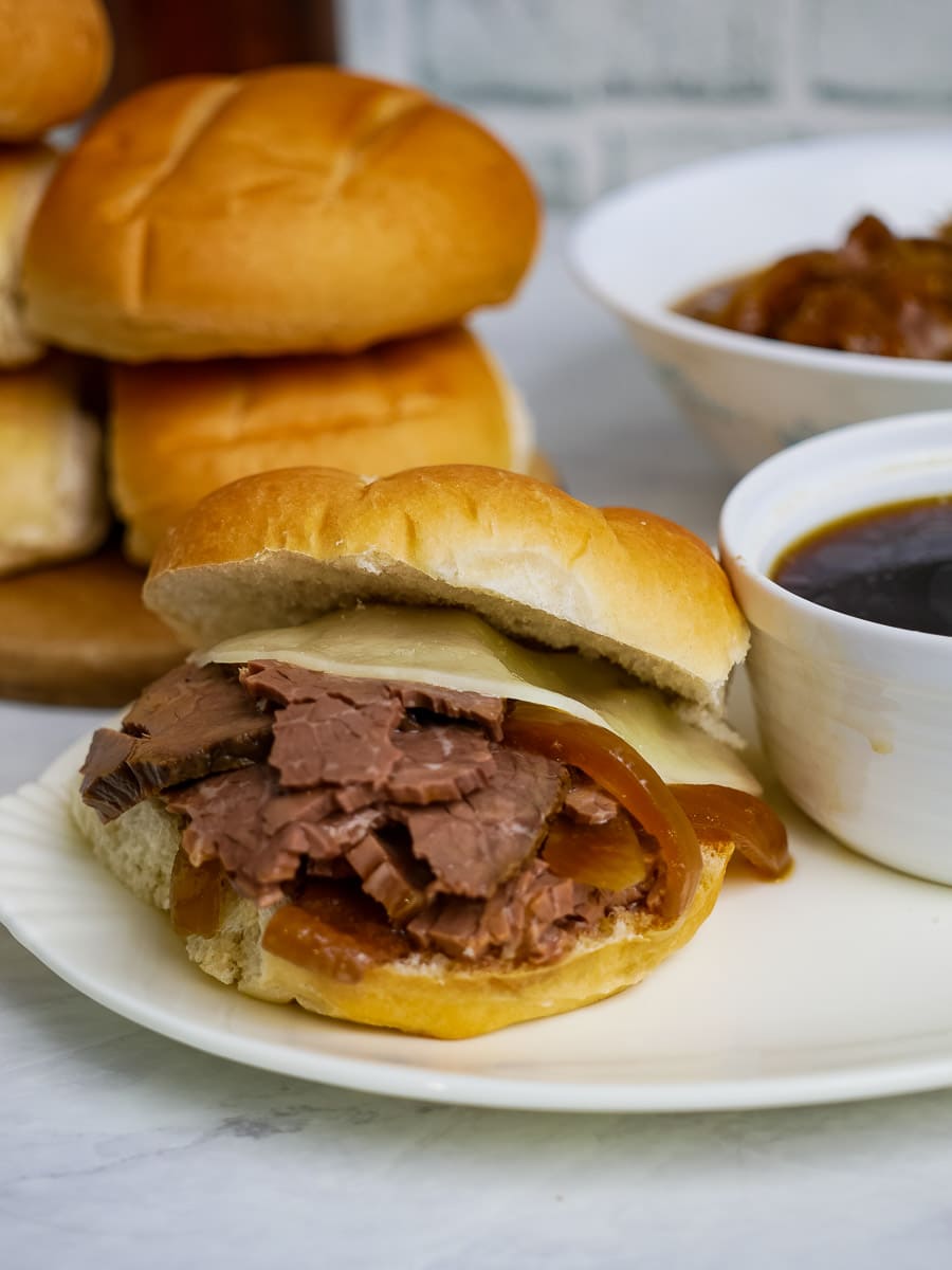 A sandwich with meat and gravy on a plate next to a bowl of sauce.