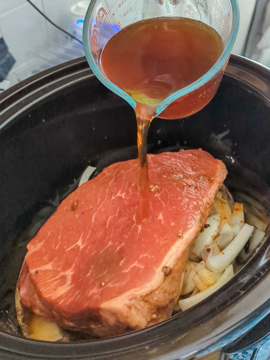 A crock pot full of meat and onions being poured with sauce.