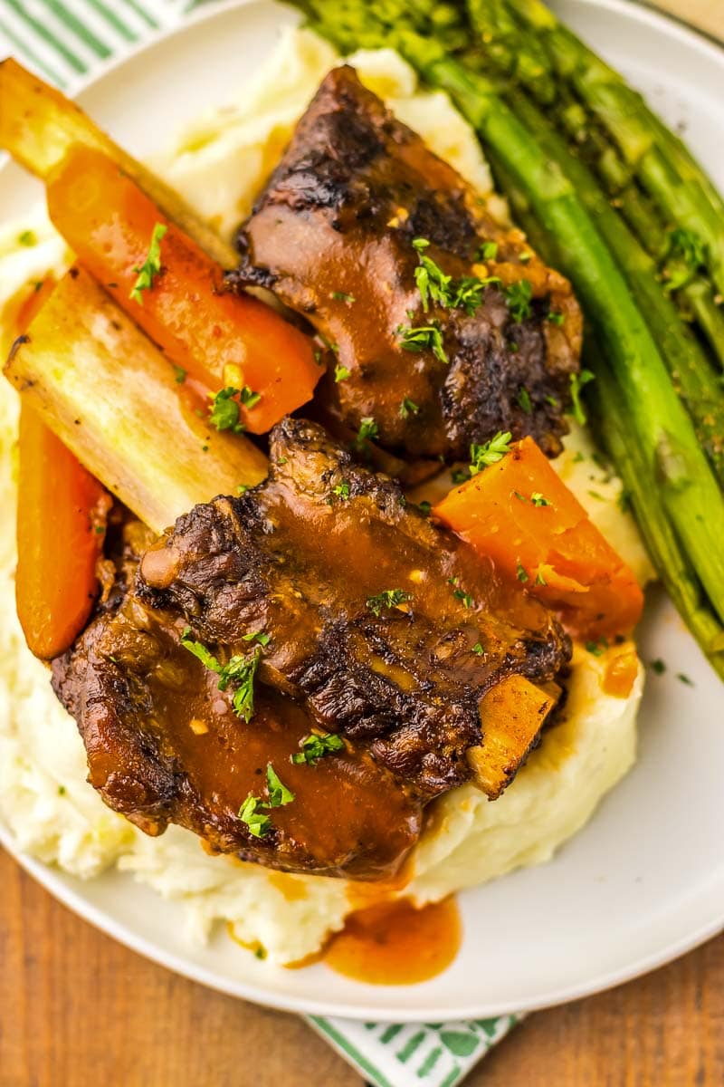A plate with ribs, mashed potatoes, asparagus and gravy.