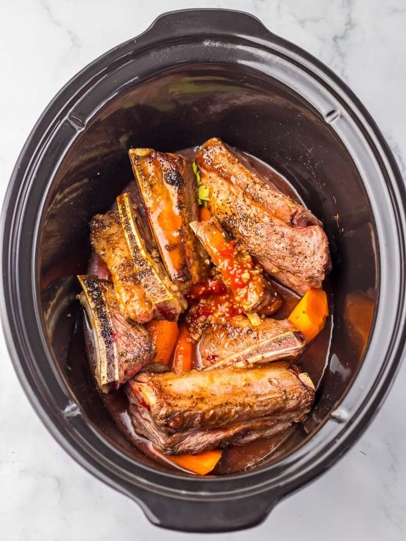 A crock pot filled with ribs and vegetables.