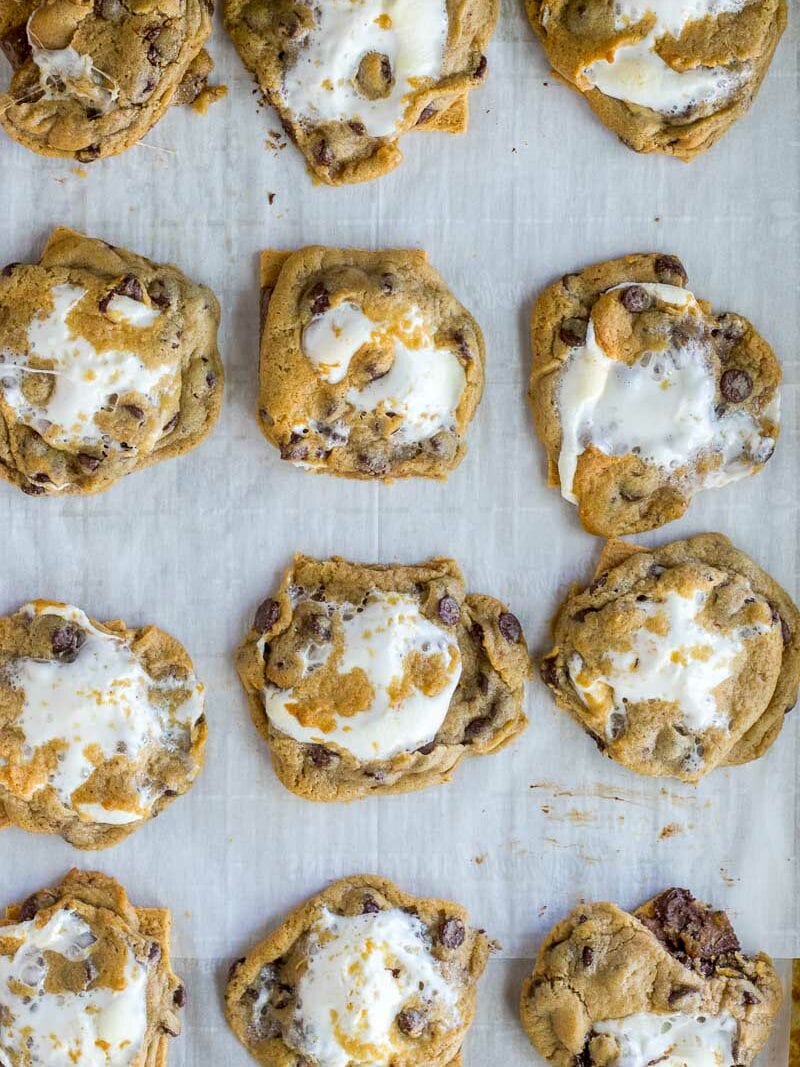 Freshly baked chocolate chip cookies with melting marshmallows on top, arranged on parchment paper.