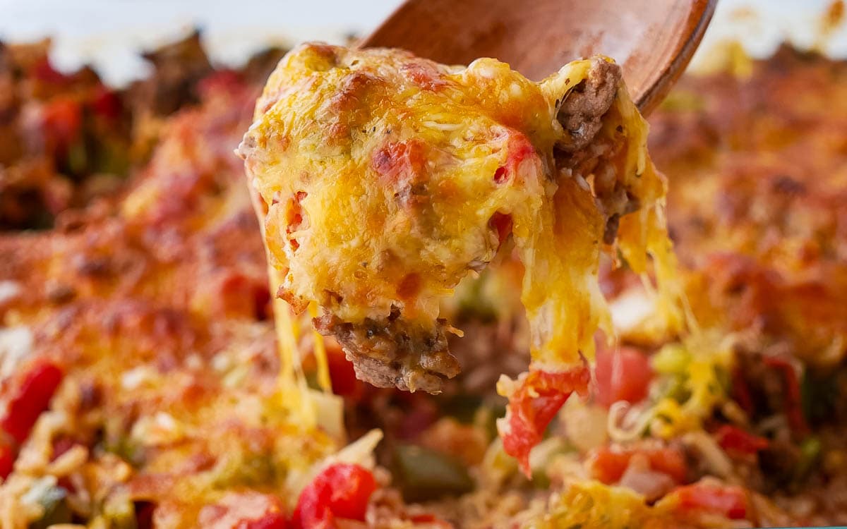 A wooden spoon is being lifted out of a stuffed bell pepper casserole dish.
