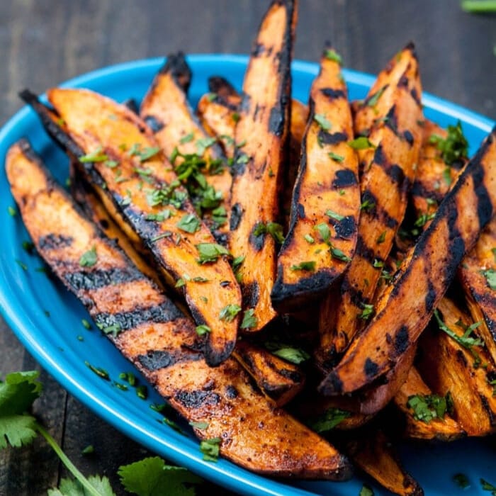 Grilled sweet potato wedges garnished with herbs on a blue plate.