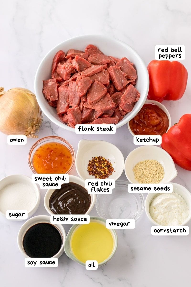 Assorted ingredients for a recipe, including flank steak and various seasonings, laid out on a kitchen counter.