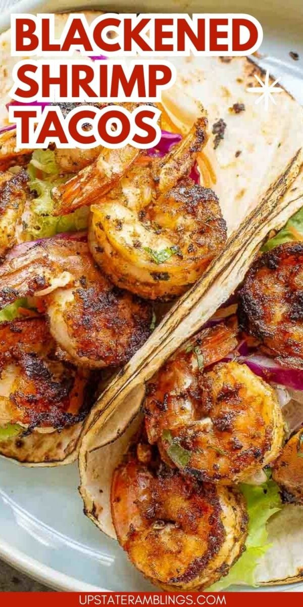 Two shrimp tacos with a spicy seasoning, filled with lettuce and red onions, served in soft tortillas.