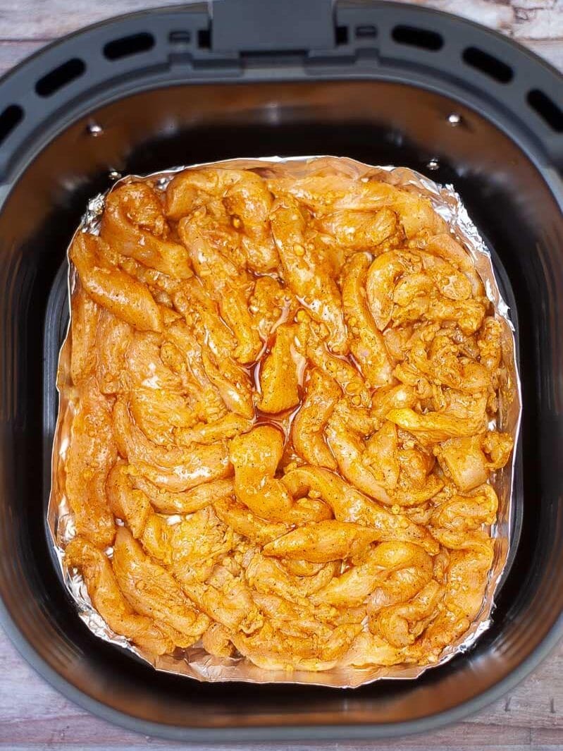 Raw seasoned chicken in foil inside an air fryer basket, ready for cooking.