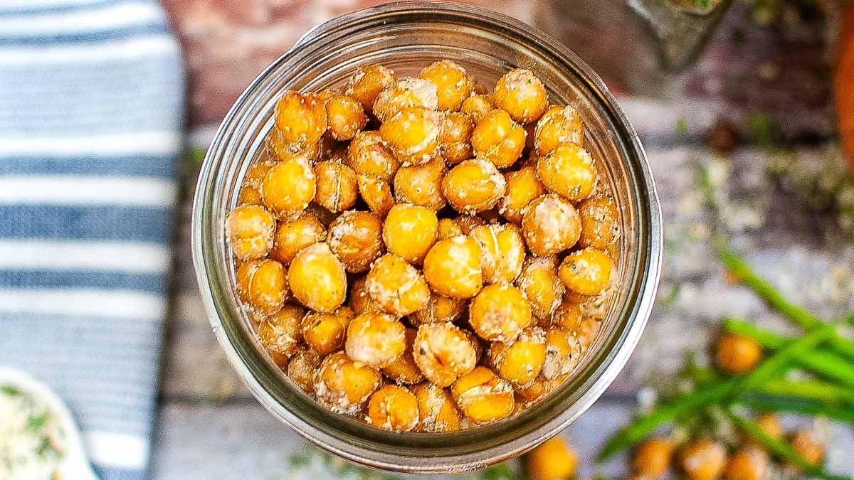 A glass jar filled with roasted chickpeas seasoned with spices, viewed from above on a rustic wooden table.