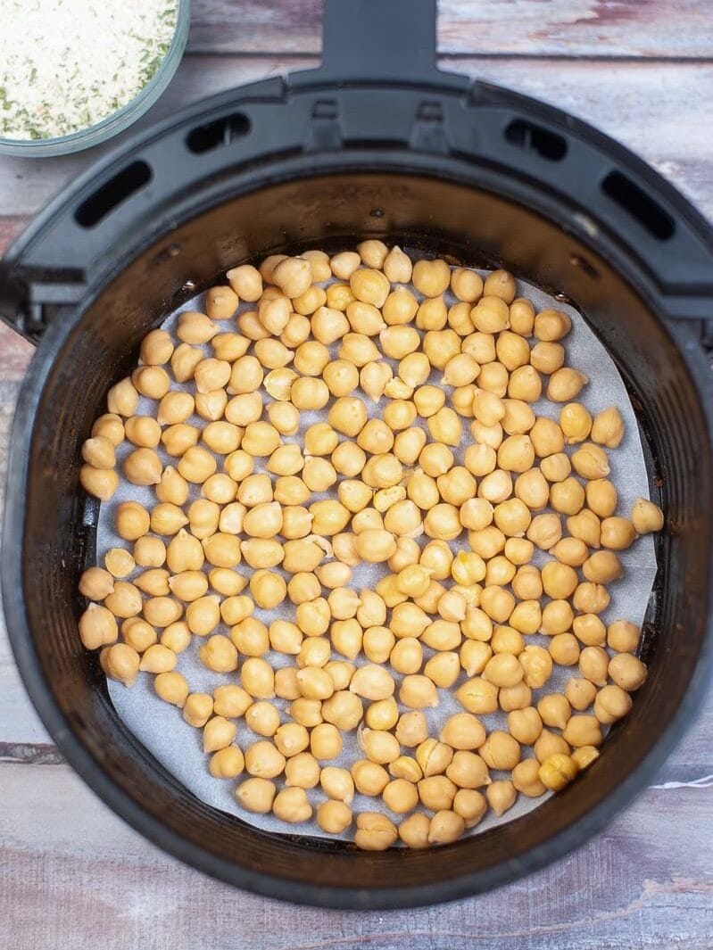 Cooked chickpeas in a black instant pot, placed on a wooden surface with a bowl of spices in the background.