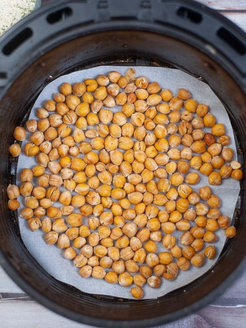 Chickpeas spread out in an air fryer basket, ready for cooking.