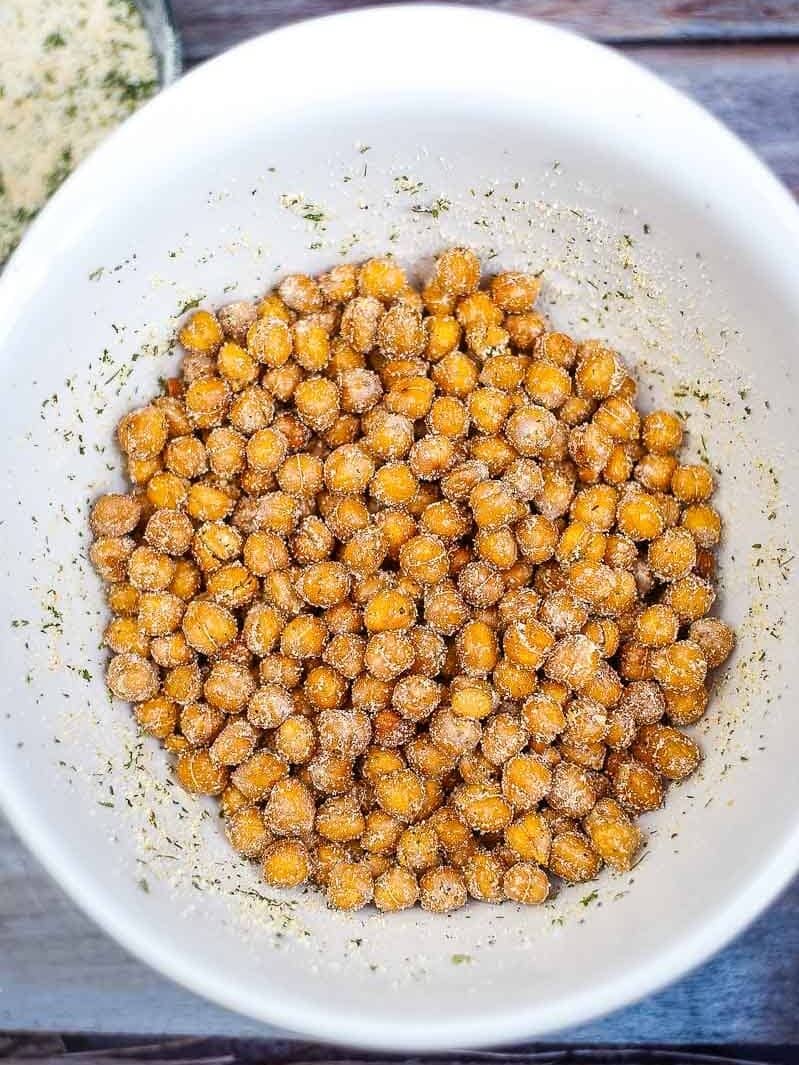 Bowl of roasted chickpeas seasoned with spices, viewed from above on a wooden surface.