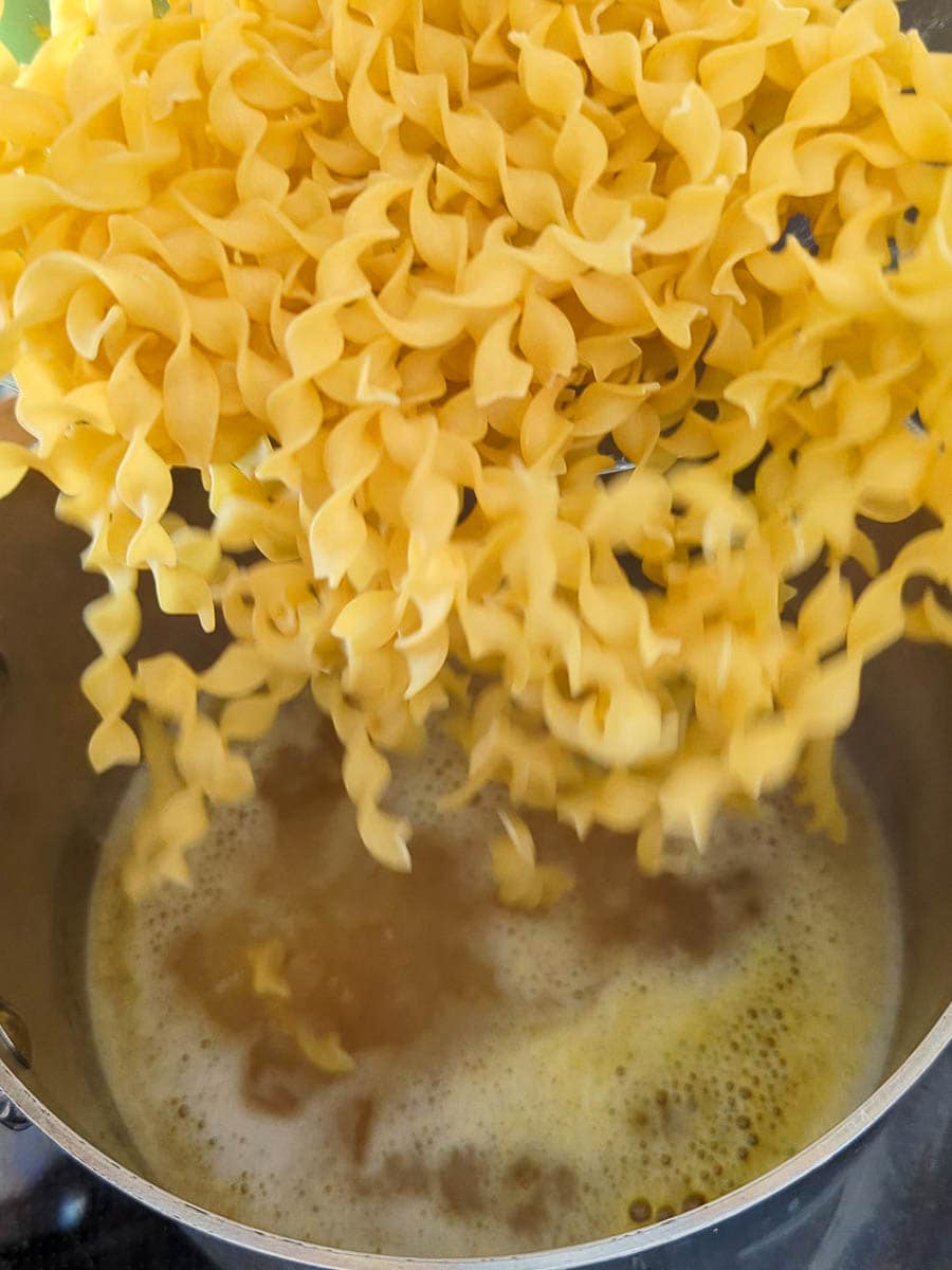 Pasta being poured into boiling water in a pot.