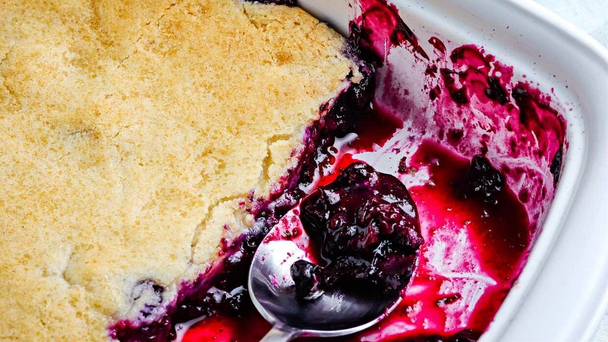 Closeup of blueberry cobbler with a few pieces gone and a spoon with berry filling.