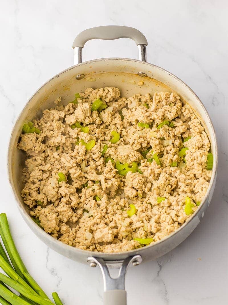 A skillet with cooked ground chicken and diced celery on a kitchen countertop.