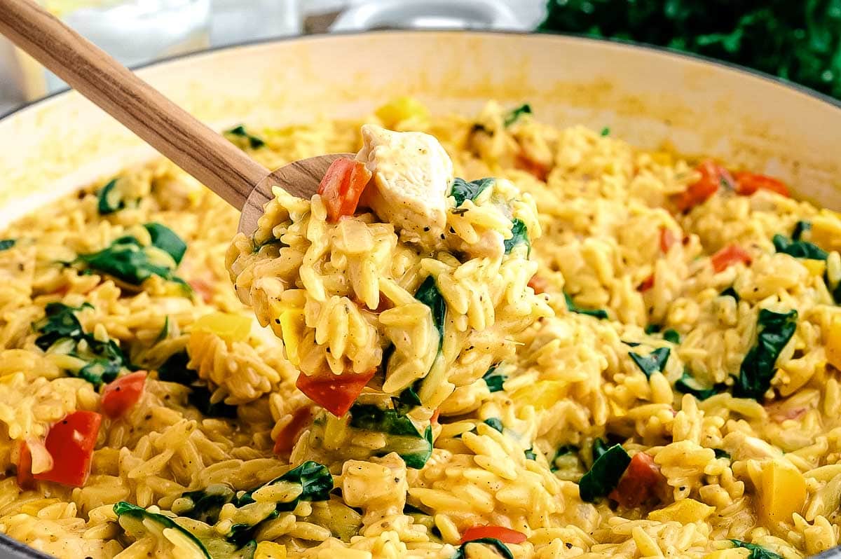 Wooden spoon lifting creamy chicken and vegetable risotto from a large pot.