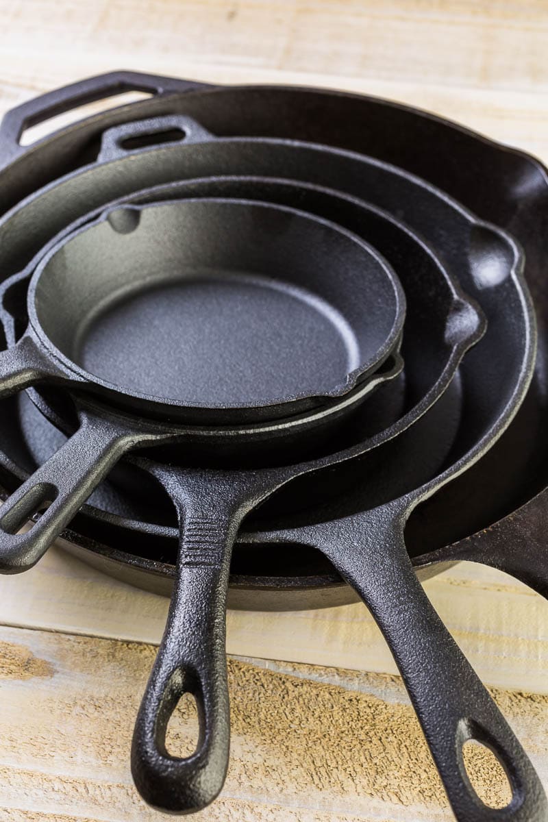 Three stacked cast iron skillets of varying sizes on a wooden surface.