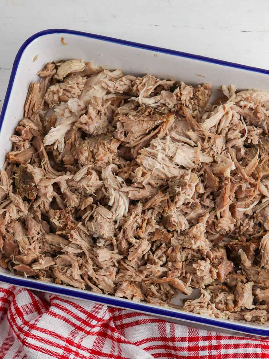 Shredded pork in a white and blue enamel baking dish on a red and white checkered cloth.