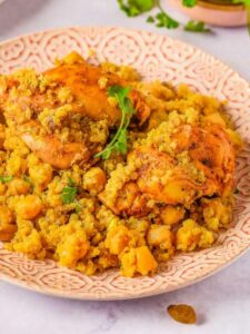 A plate of quinoa and chickpea pilaf topped with seasoned chicken thighs garnished with parsley, served on an ornate plate.