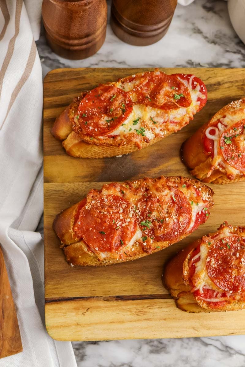 Bruschetta with melted cheese and pepperoni on a wooden board, accompanied by salt and pepper shakers.