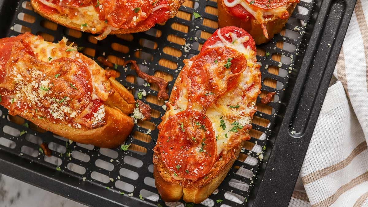 Slices of french bread pizza topped with melted cheese, tomato slices, and herbs on a cooling rack.